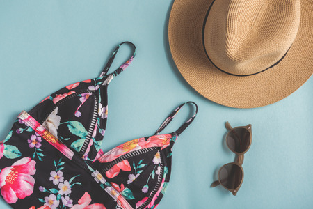 Bright swimsuit is locating near sunglasses and hat on blue surface. Top view. Nobody. Close upの写真素材