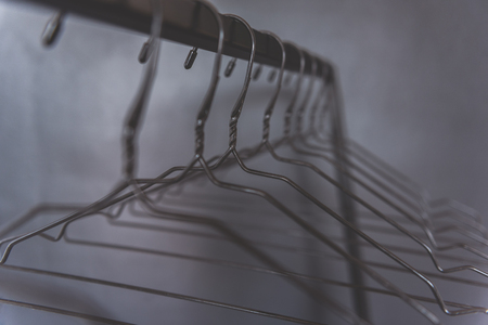 Empty hangers are hanging at cross-bar near grey wall. Close up of shaped wires. Copy space. Nobodyの写真素材