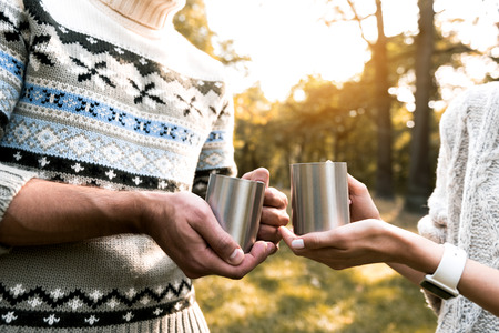 Close up of arms of loving couple enjoying hot tea together in the forest. They are standing and...