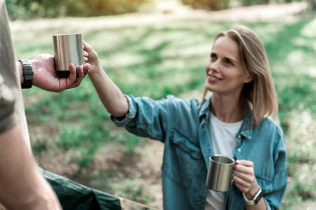 Joyful wife handing hot beverage to husband in forestの写真素材