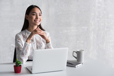 Dreamy smiling businesswoman sitting near deskの写真素材