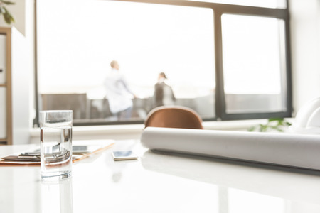 Close up of glass with water is on desk near other necessary things. People standing on balcony at background. Copy space on right sideの写真素材