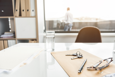 Eyeglasses near keys and pen are on folder for documents. Glass of water at countertop. Man is on background. Copy space on right sideの写真素材
