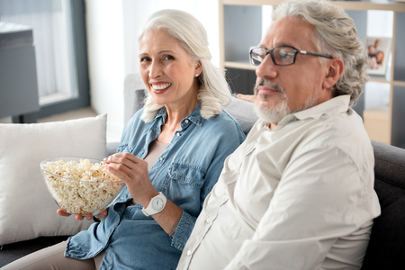 Cheerful senior married couple watching television at homeの写真素材