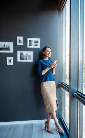Positive elegant businesswoman is standing with mobile phoneの写真素材