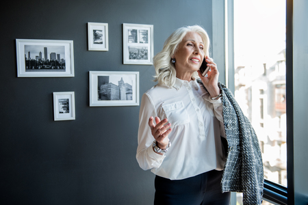 Attractive joyful old lady is communicating using smartphoneの写真素材