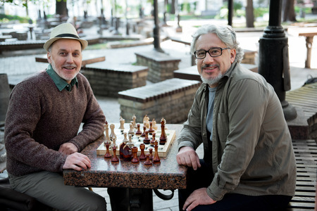 Glad mature pensioners relaxing near chessboard in parkの写真素材