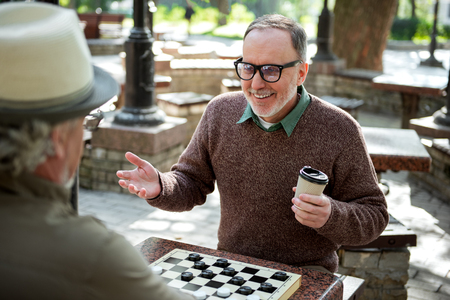 Cheerful mature male pensioners entertaining with draughts in parkの写真素材