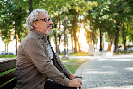 Glad male pensioner relaxing in the nature with hot drinkの写真素材