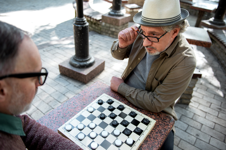 Pensive senior male pensioners playing chequers