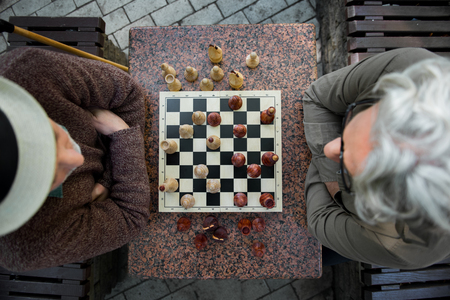 Pensive old male pensioners looking at chessboard with concentrationの写真素材