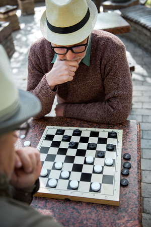 Pensive senior man playing chequers with his friendの写真素材