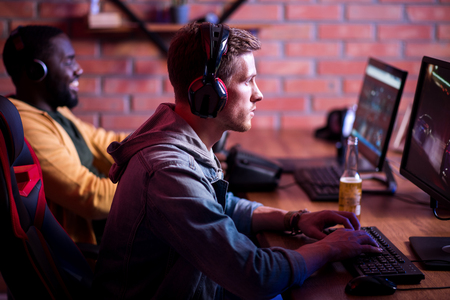 Favorite hobby. Selective profile of concentrated young gamer in headphones is sitting in computer...