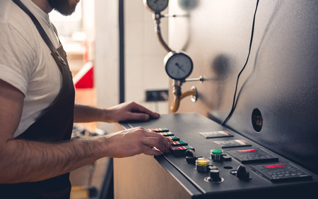 Bearded male master pressing button on special equipment for creating coffee. Technical appliance concept. Close up of his handの写真素材