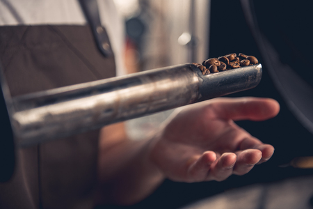 Close up arm of master checking different degrees of roasting coffee with special scapula stick. Monitoring conceptの写真素材