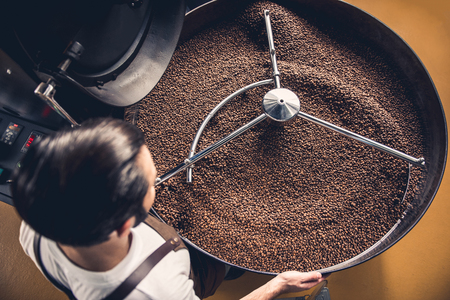Top view coffee roaster worker controlling beans falling into spinning cooler professional machine. Arabica conceptの写真素材