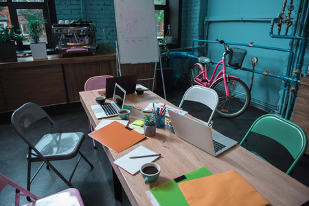 Cozy room. Modern empty office of creative young team with big table and colored chairs around it. Coffee machine with flipchart and pink bicycle in backgroundの写真素材
