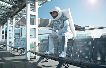 Spaceman wearing white uniform is sitting on bench and looking ahead with seriousness. Low angle. Copy space on right sideの写真素材