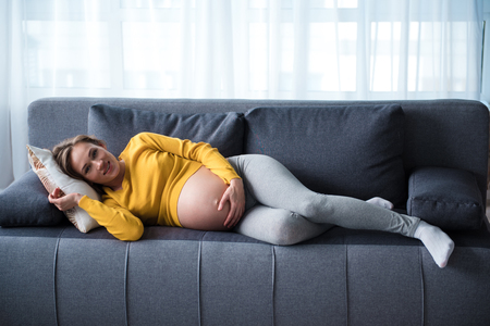 Portrait of cheerful pregnant woman relaxing on couch at home. She is looking at camera and smilingの写真素材