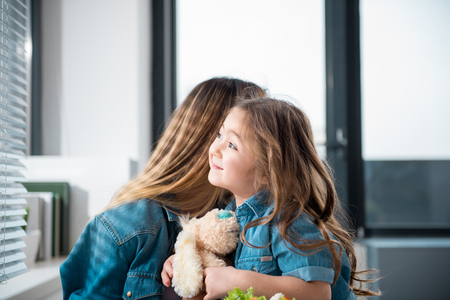 Side view of happy asian girl enjoying hug of her mother. She is holding soft toy and smilingの写真素材
