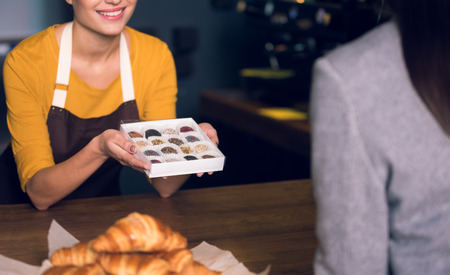 Close up seller hands holding appetizing candies. She demonstrating them to client. Cafe conceptの写真素材
