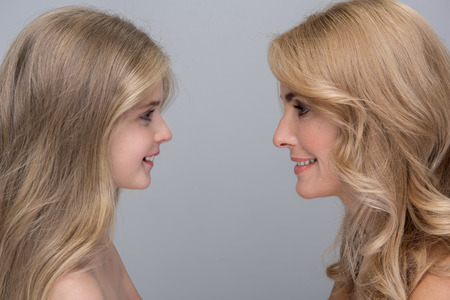 My little princess. Side view profile of cheerful mother and her pretty daughter are standing and looking at each other with love. They are feeling happiness while spending time together. Isolatedの写真素材