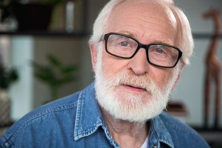 Close up portrait of pensive old bearded man looking at camera. He expresses sincerity, openness...
