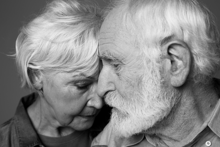 Close up black-and-white portrait of grey-haired man and woman standing closely. Isolated on grey backgroundの写真素材