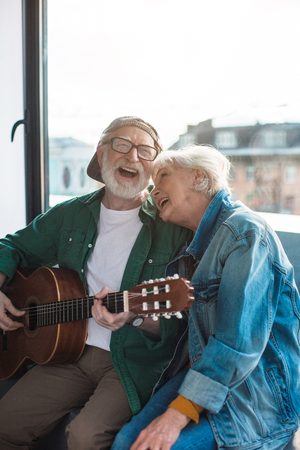 Merry aged man and woman spending holiday while playing on guitar and singing at home. Portraitの写真素材