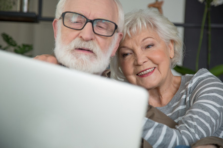 Close up portrait of smiling pensioners talking with family through computer. Focus on woman putting hand on male shoulderの写真素材