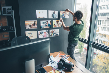 Serious bearded man ornamenting wall by different images while standing in office. Labor and design conceptの写真素材