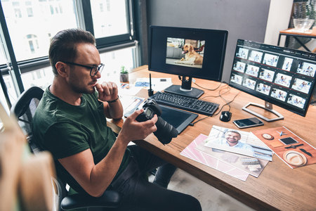 Top view serene bearded photographer watching at camera while holding it in arms in office. Image conceptの写真素材