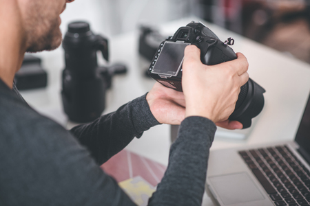 Top view close up male hands holding digital device for taking photos. He looking at screen of it at desk. Image conceptの写真素材