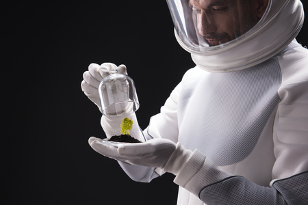 New organism. Close-up of hands of curious skilled male astronaut wearing helmet and protective suit is standing and discovering alien forms of life while expressive interest. Isolated backgroundの写真素材