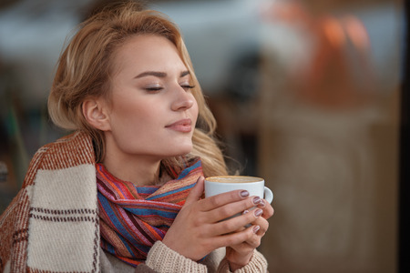 Pleasant flavor. Waist up portrait of young lady in blanket enjoying favorite drink at cafe. Copy...