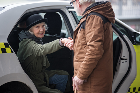 You are so kind. Old man is helping elegant senior woman to get out of taxi. She is looking at him gratefully. Focus on femaleの写真素材