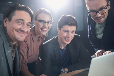 Portrait of cheerful males and beaming woman working with notebook computer while situating at desk in room. Profession and career conceptの写真素材