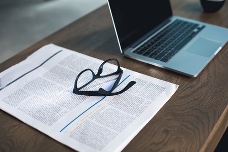 Newspaper, glasses and modern notebook computer situating on wooden table in apartment. Design and occupation conceptの写真素材