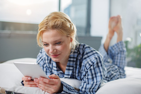 Waist up portrait of calm female relaxing at home. She is looking on pad screen