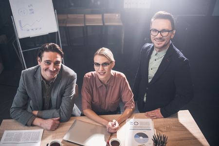 Top view portrait of happy male telling with cheerful female colleague while situating at desk in office. Communication and business conceptの写真素材