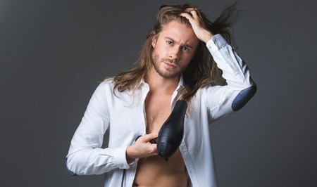 Waist up portrait of severe guy blow drying hair. Isolated on grey backgroundの写真素材