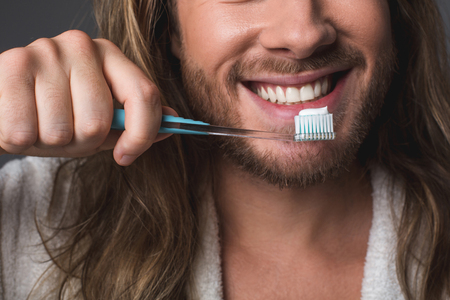 Oral hygiene. Close up of smiling guy holding toothbrush with toothpaste on topの写真素材