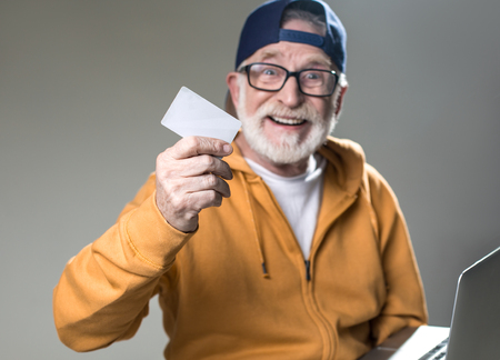 Waist up portrait of bearded gaffer with happy face holding credit card. Isolated on grey...