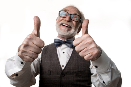 Excellent. Waist up portrait of grayhaired balding senior man holding his thumbs up and smiling. Focus on hands. Isolated on backgroundの写真素材