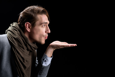 Air-kiss. Side view profile of elegant trendy young positive man is standing and holding palm up...