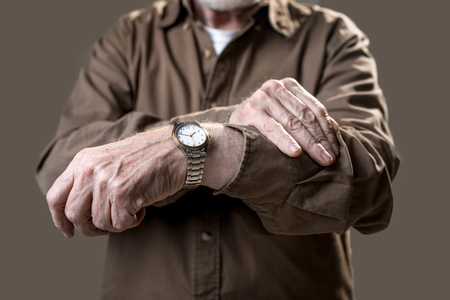 Man checking time on his wristwatch while showing it to camera. Isolated on grey background. Close upの写真素材