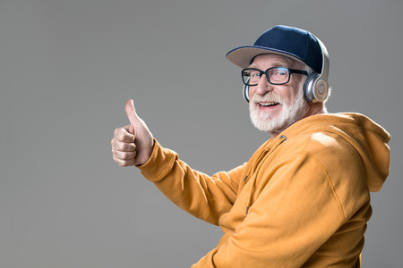 Stylish happy gaffer with headphones on head. His gesture expressing enjoyment. Isolated on grey...