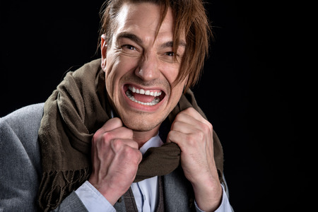 Portrait of irritated young man is standing and feeling anger while yelling loudly. He is looking at camera with aggression and fury while holding his collar. Isolated backgroundの写真素材