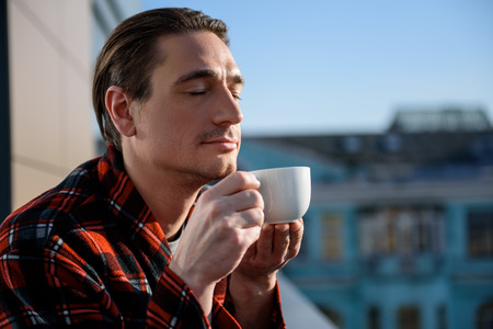 How it smells. Portrait of calm guy standing outside and holding a cup, he is smelling drink with closed eyes. Copy space in right sideの写真素材