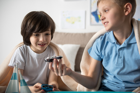 Happy juvenile boy showing toy car to his friend, boy is looking at it with admirationの写真素材